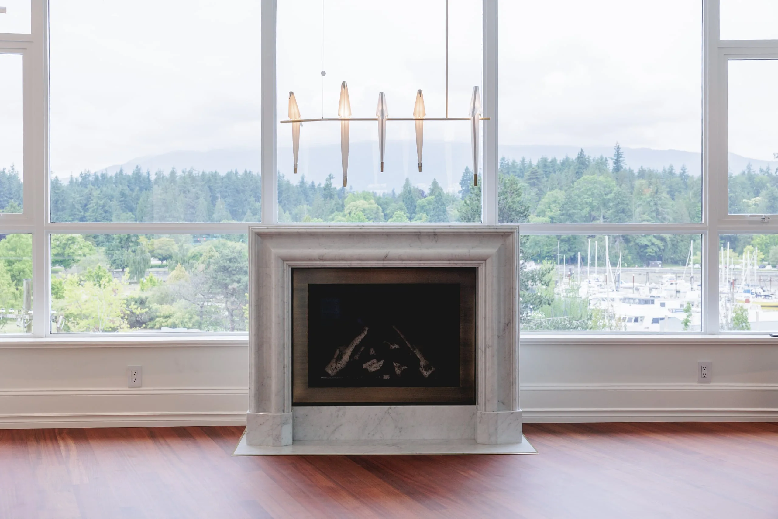 A marble fireplace in a renovated Coal Harbour condo, with the harbour and the North Shore beyond the windows.