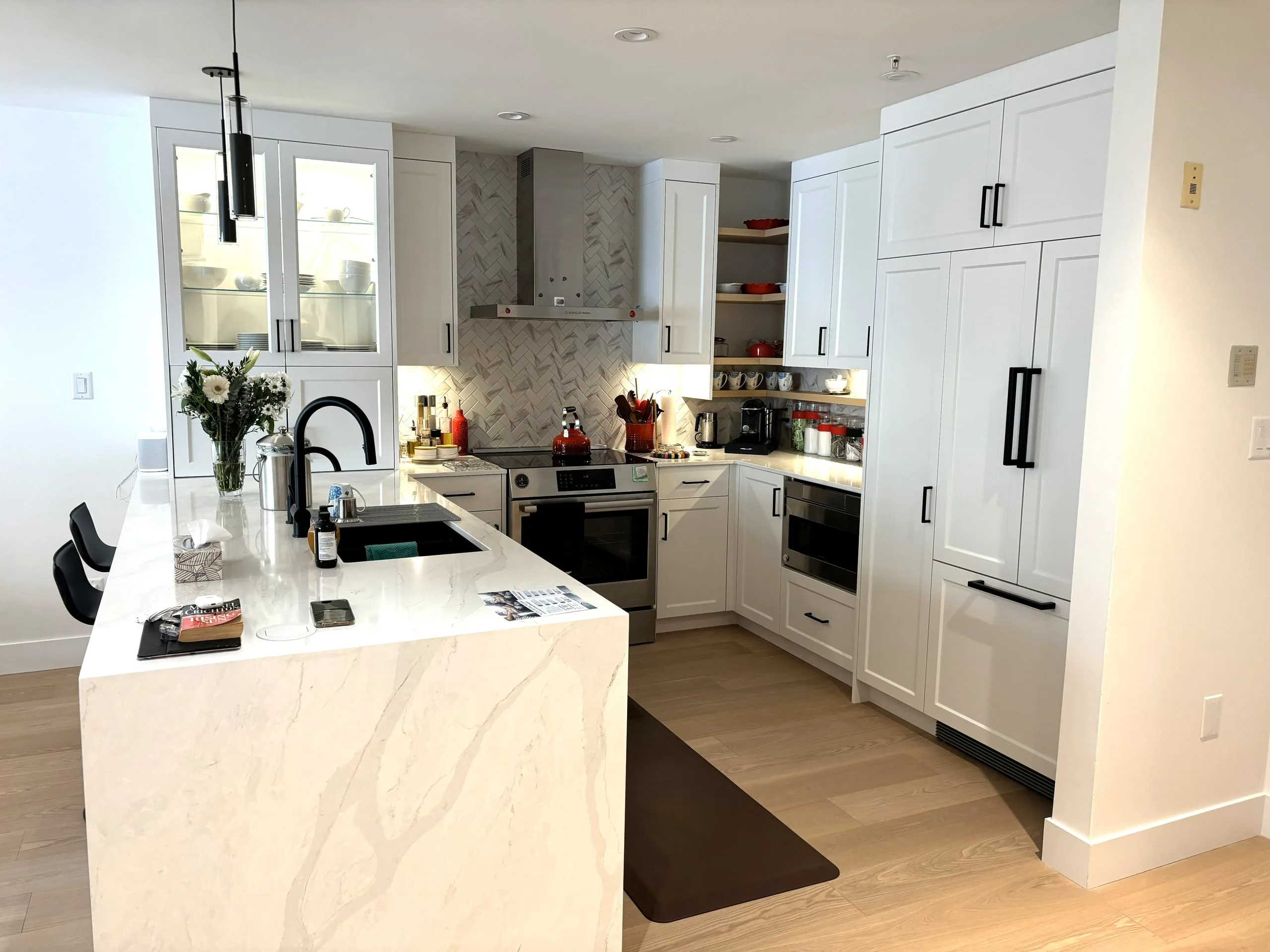 The reconfigured condo kitchen, with a waterfall quartz island, white shaker cabinets and black pendants.