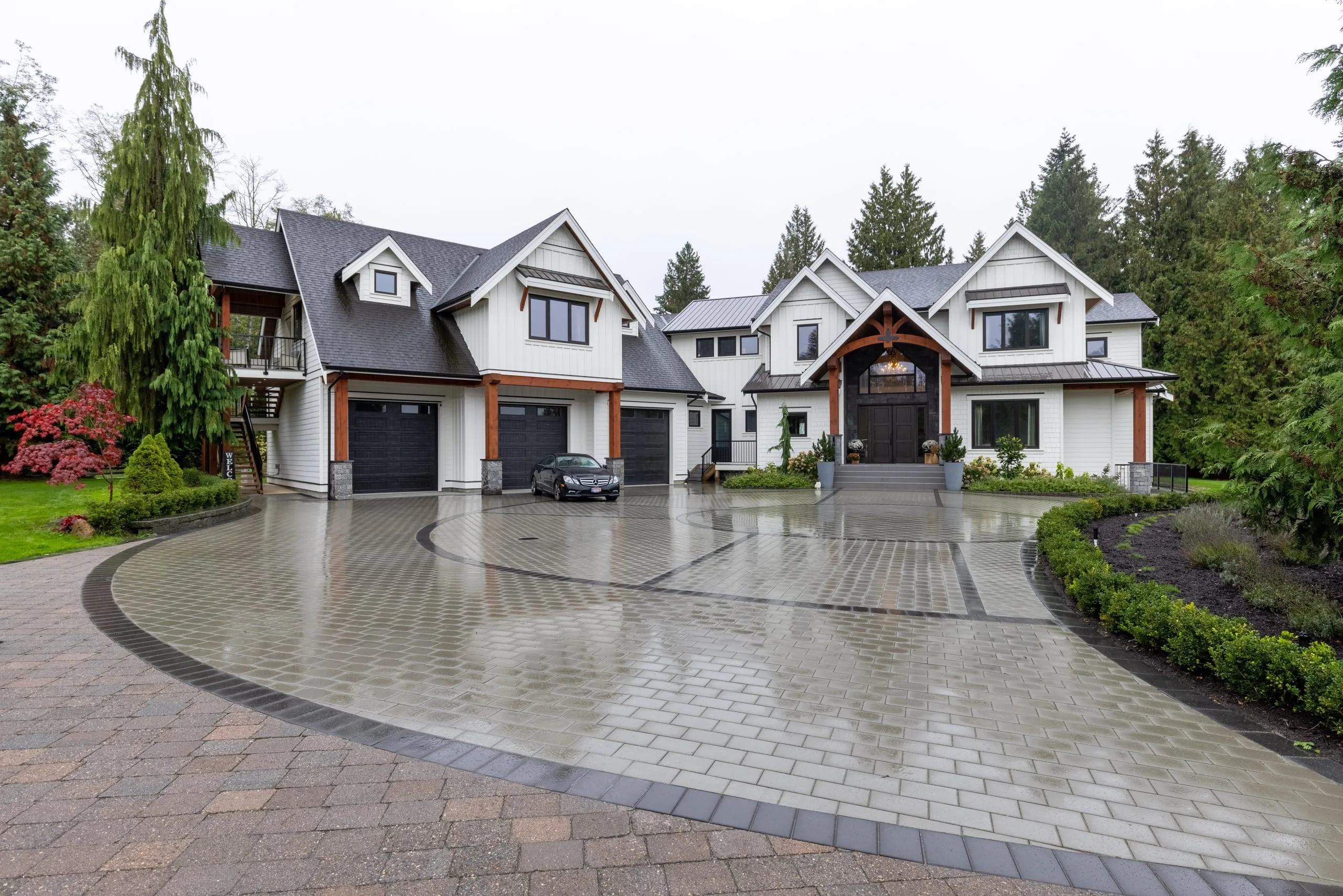 The front of a custom home in Langley: white board-and-batten wings, a heavy-timber gable entry and a circular paver court.