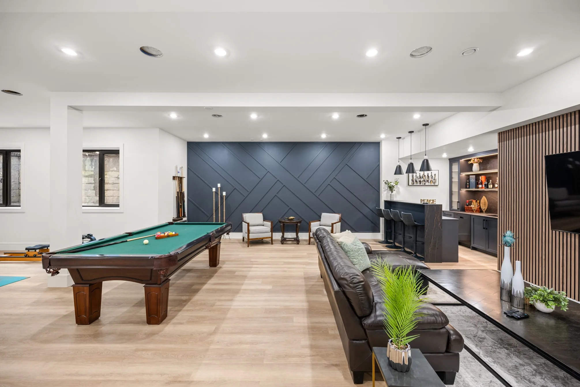 A finished basement in Langley: a pool table in front of a navy panelled feature wall, a leather sectional and the wet bar.
