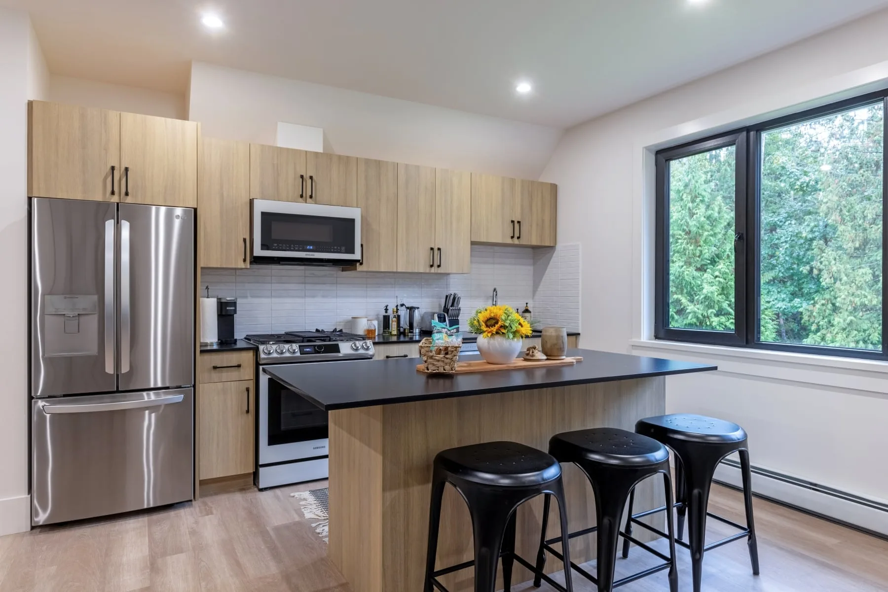The coach house kitchen, with an oak-and-black island, black stools and a window onto the trees.