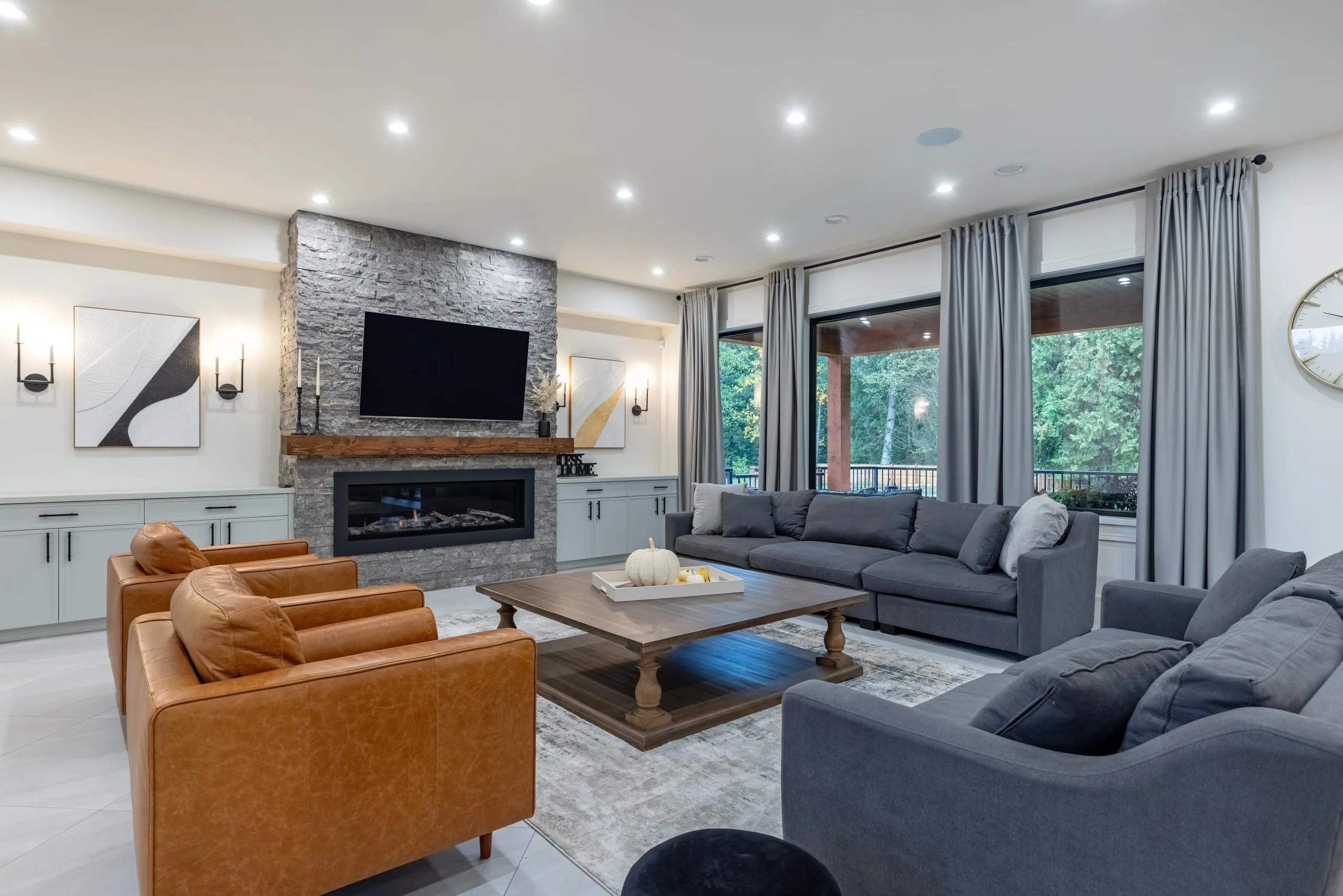 The great room of the Modern Country Estate, with a stacked-stone fireplace wall and cognac leather chairs.