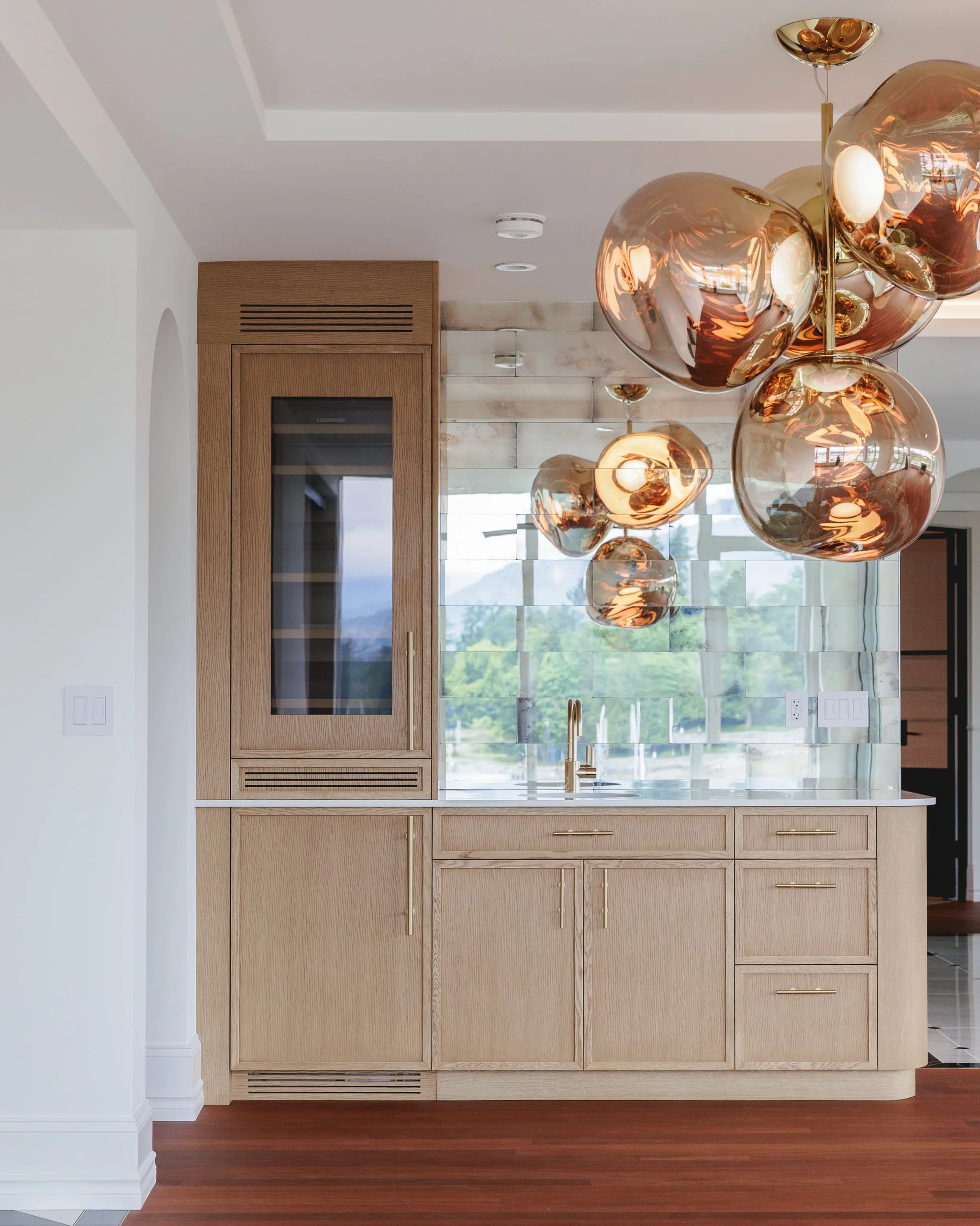 A bar niche in white oak under copper globe pendants, with the harbour view through the window.