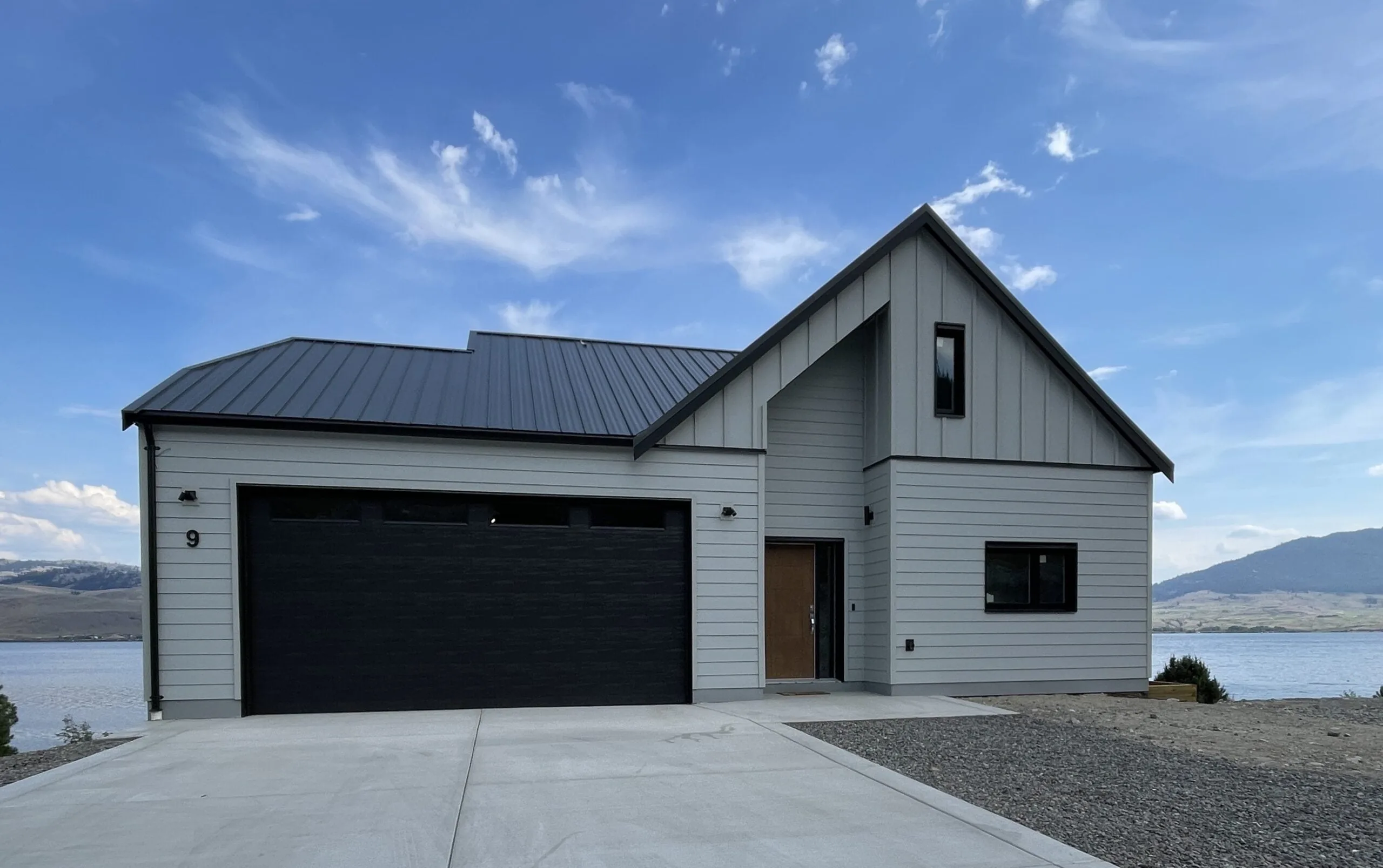 The finished lake house, with white board-and-batten siding, a black metal roof and a double garage.