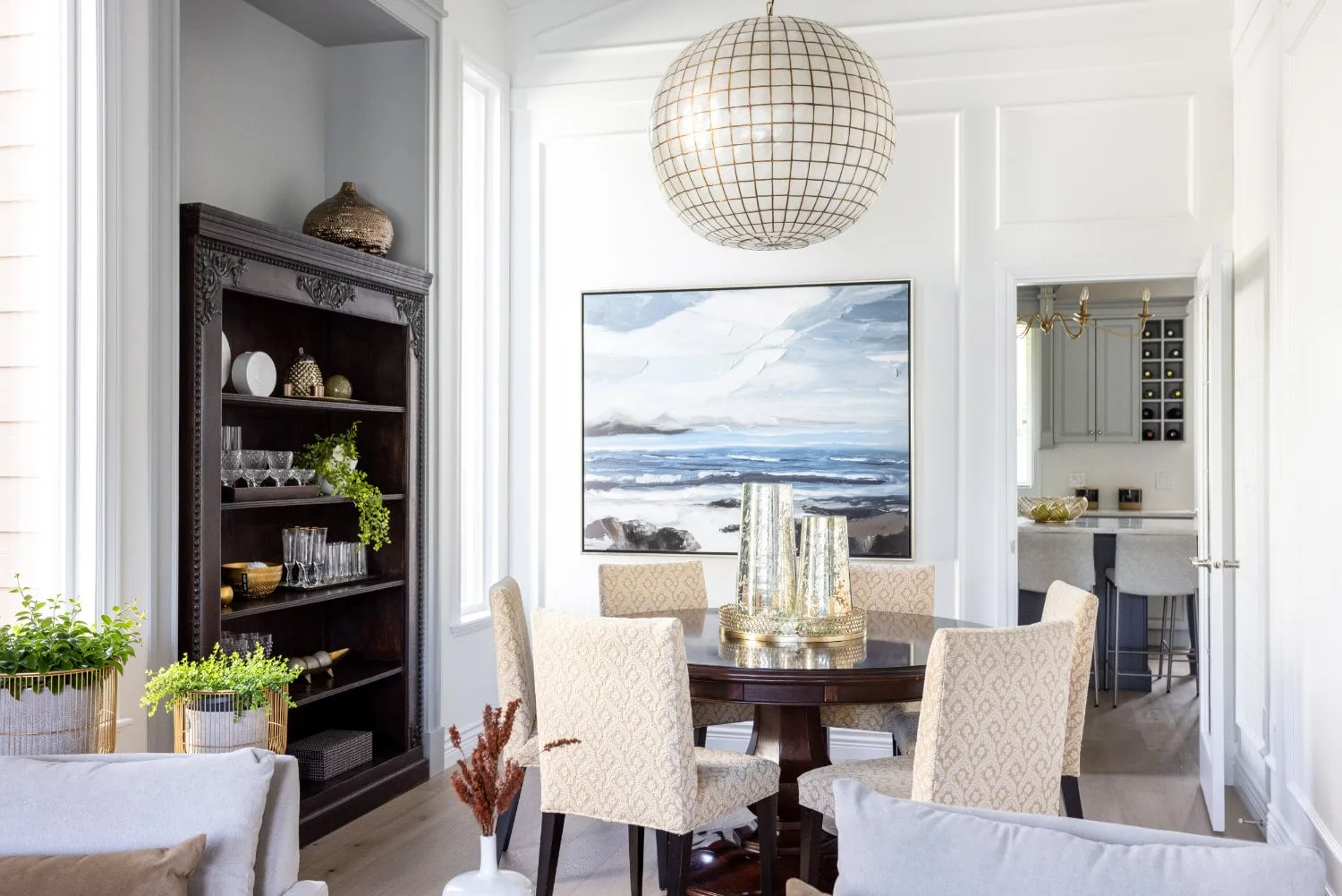 The dining room of the Modern Classic Residence in South Surrey, with a globe pendant, a round table and a dark bookcase.
