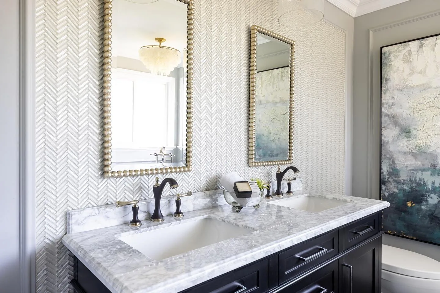 The ensuite vanity of the Modern Classic Residence in South Surrey, with a herringbone tile wall, brass mirrors and a navy cabinet.