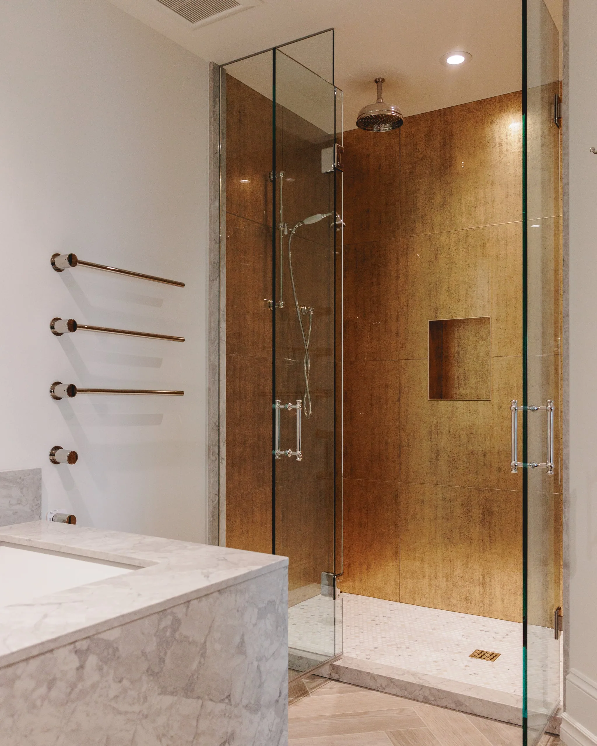 A glass shower lined in gold-leaf tile with a marble tub deck, in a renovated Coal Harbour condo.