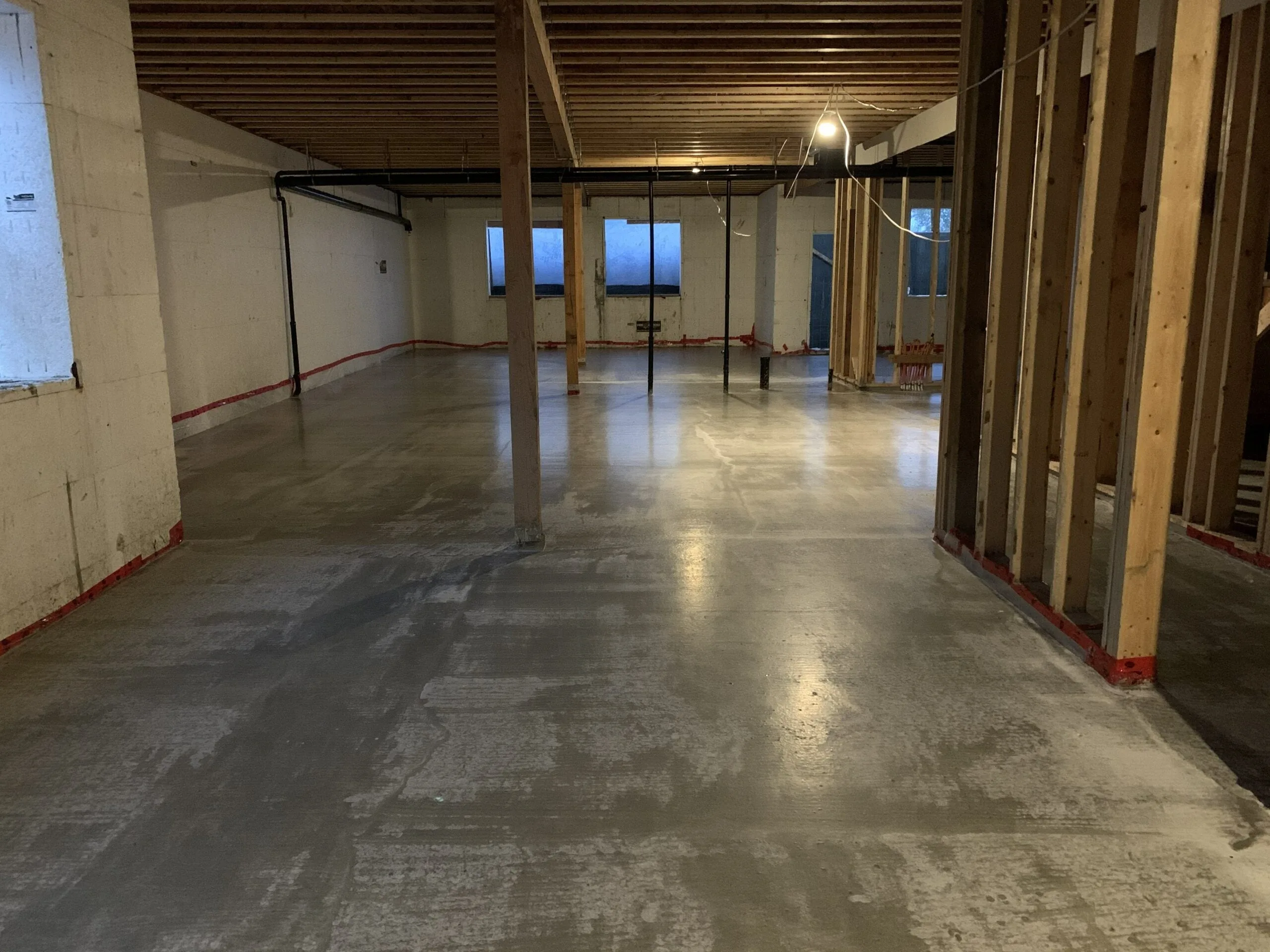 A basement stripped back to bare studs and open joists over a concrete floor.