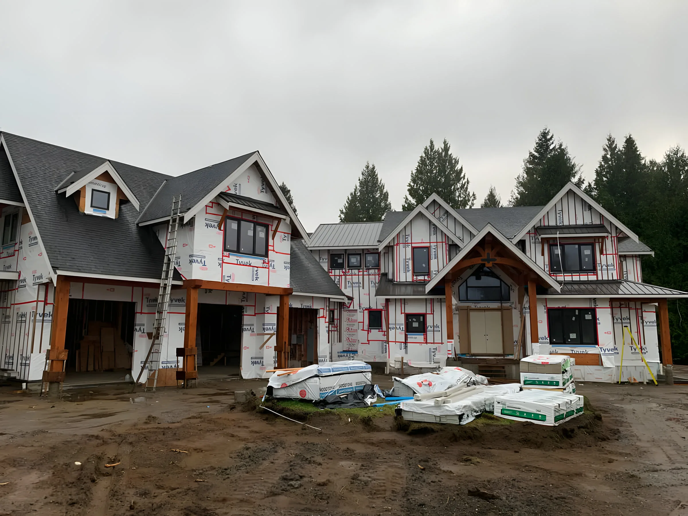 A house mid-build, wrapped and framed, with materials stacked on the lot.