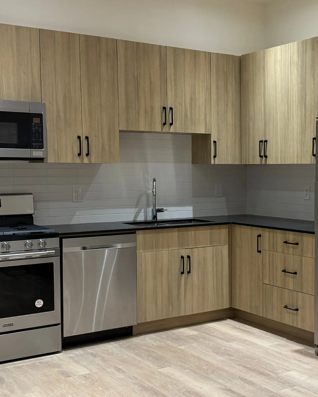 After: the finished suite kitchen, with wood-look cabinets, a stainless range, microwave and dishwasher, and a grey tile backsplash.
