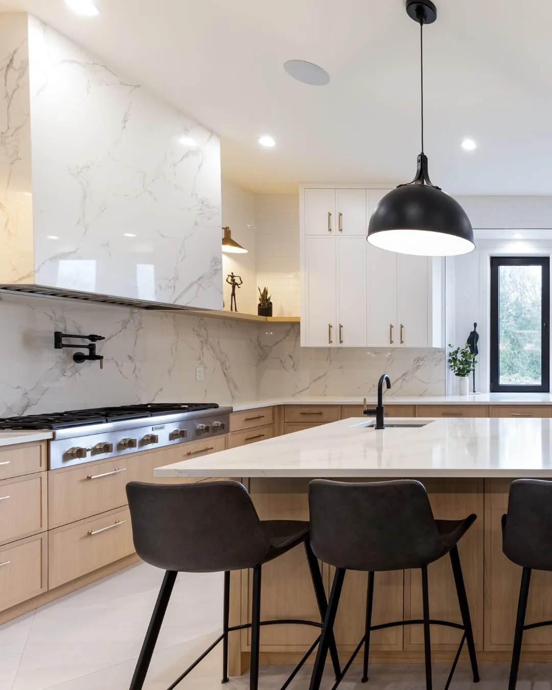 Finished: the finished kitchen, with a marble slab range wall, a gas range, white-oak cabinets, a quartz island and a black dome pendant.
