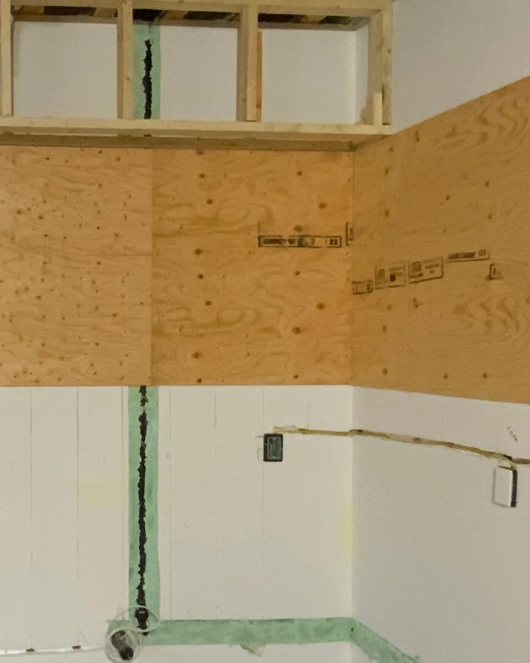 Before: the kitchen wall before the work: open framing, plywood and bare wiring.