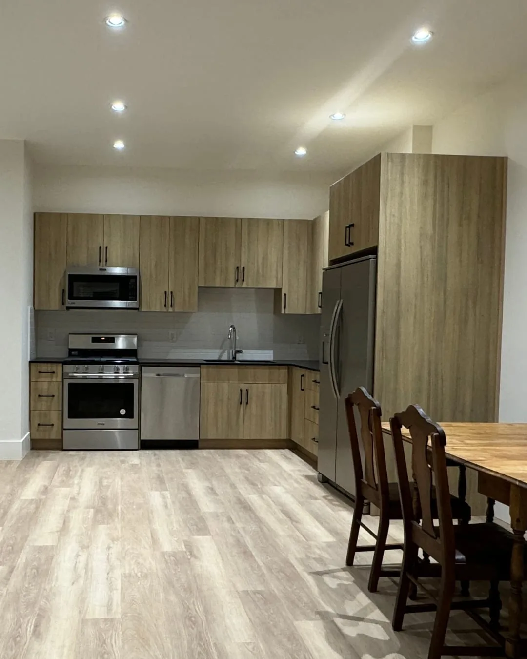 After: the finished kitchen and dining area, with pot lights, laminate flooring and a full-height fridge cabinet.